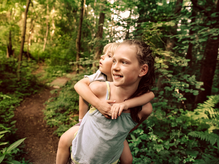 Young girl carries her sister on her back for a walk through the woods