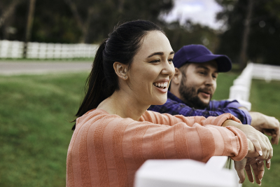 A woman and man leaning on a fence outside