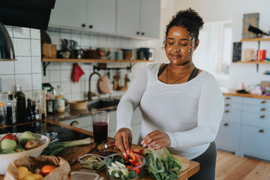 Una mujer de pie en una cocina con un mostrador lleno de frutas y verduras